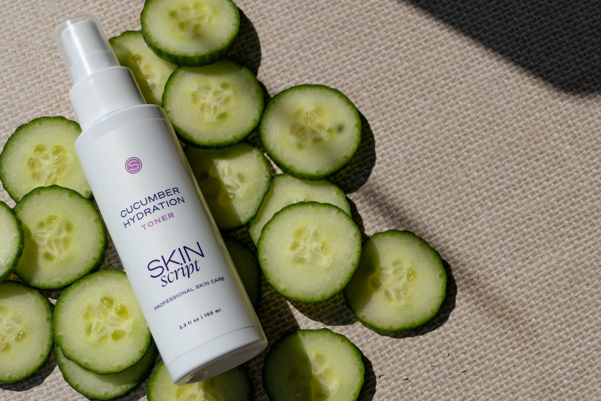 Skincare toner bottle labeled 'Skin Script' with sliced cucumbers on a textured surface