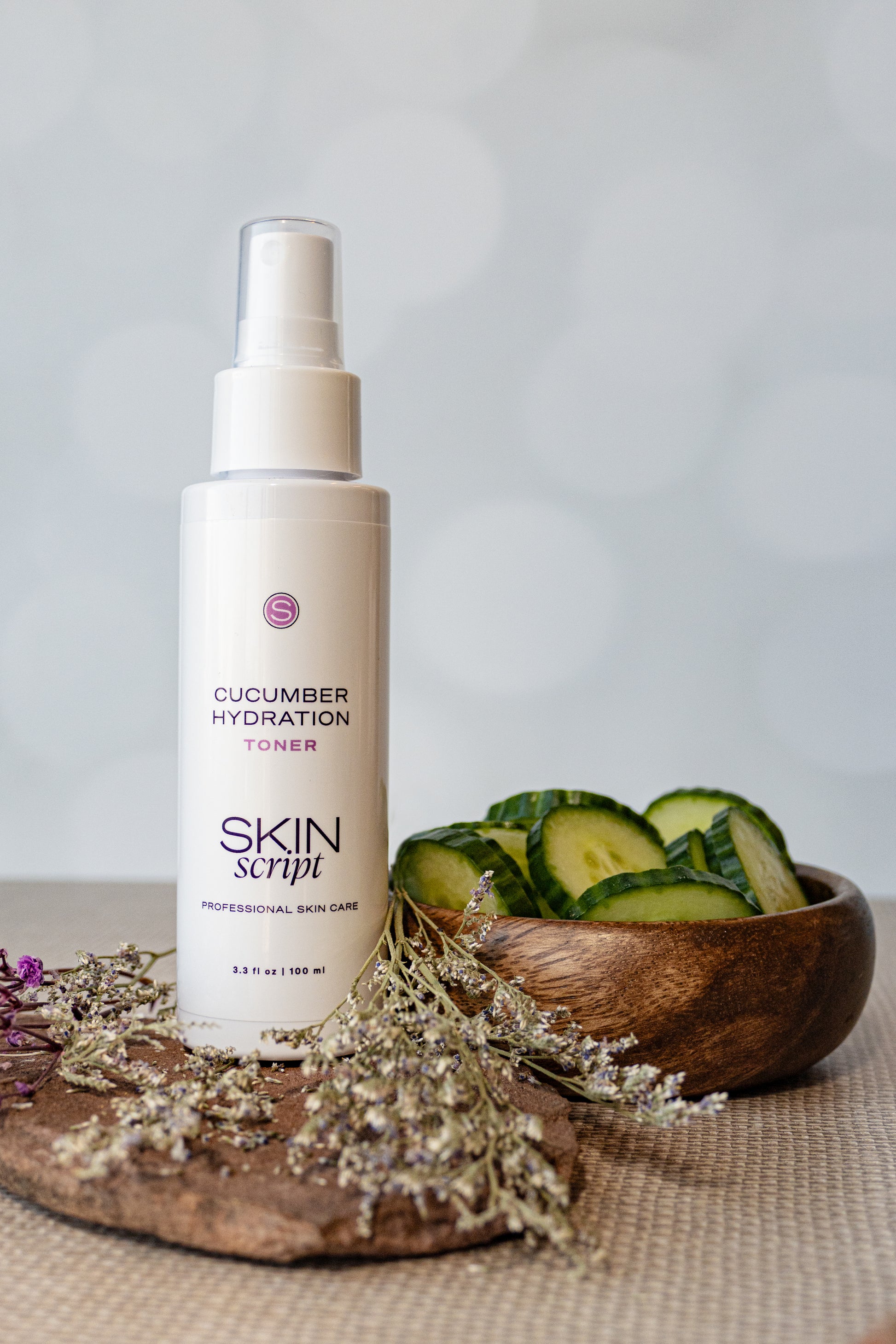 Skincare bottle labeled 'Cucumber Hydration Toner' by Skin Script on a neutral background with cucumbers.