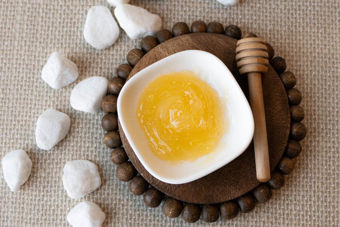 Melted skin script honey mask in a white dish on a wooden coaster with stones and a honey dipper.