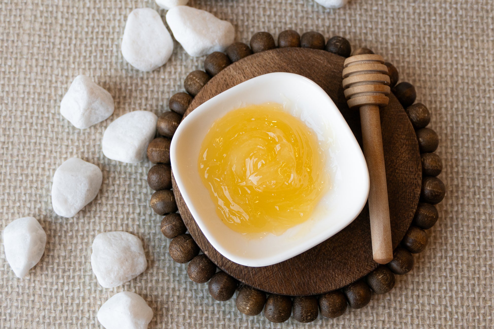 Melted skin script honey mask in a white dish on a wooden coaster with stones and a honey dipper.