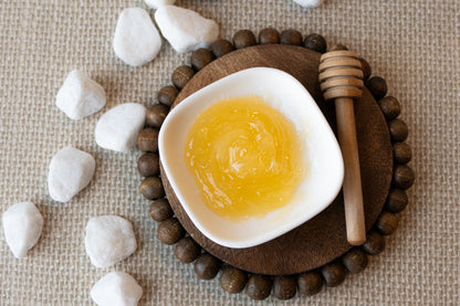 Melted skin script honey mask in a white dish on a wooden coaster with stones and a honey dipper.